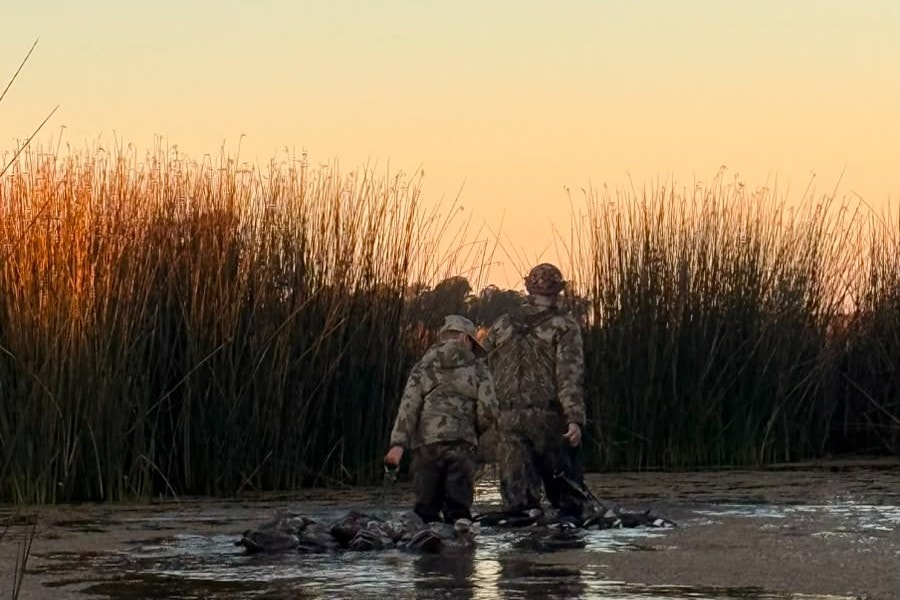 Three hunters with a large morning's bag of ducks by the water